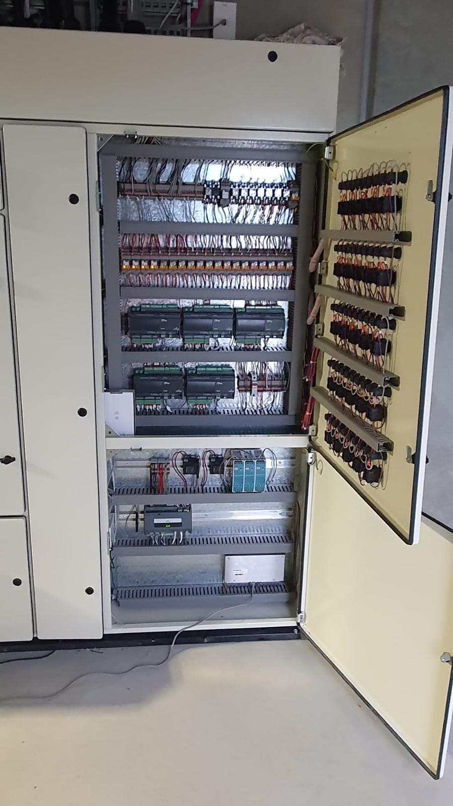 Open BMS control panel with controllers, relays, and wiring mounted in a cabinet
